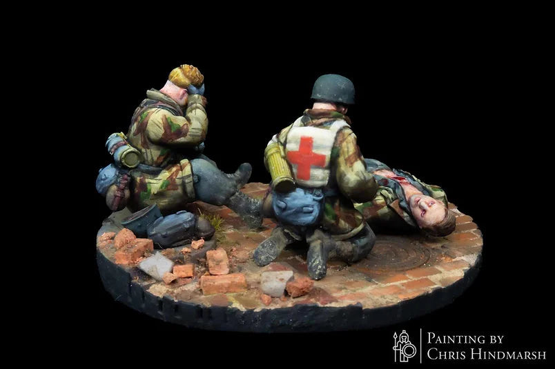 Scène d'évacuation sanitaire avec un médecin de combat allemand, figurine d'élite pour scénarios Bolt Action, détails du camouflage et du matériel de premier secours.