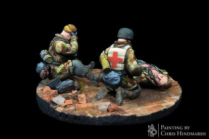Scène d'évacuation sanitaire avec un médecin de combat allemand, figurine d'élite pour scénarios Bolt Action, détails du camouflage et du matériel de premier secours.